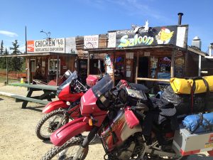 Image of two motorcycles parked outside of a building that includes the town saloon and grocery store.