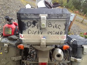 Image of the back of a motorcycle covered in mud and dirt where someone wrote in the dust "Dirty Bike Dirty Mind"
