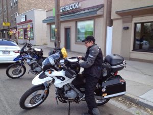 Image of Judy standing next to her motorcycle outside of several shops