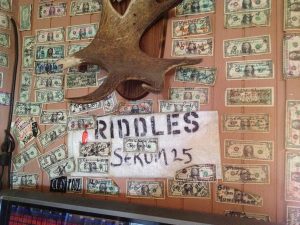 Image of many dollar bills with writing attached to a wall with antlers in the middle